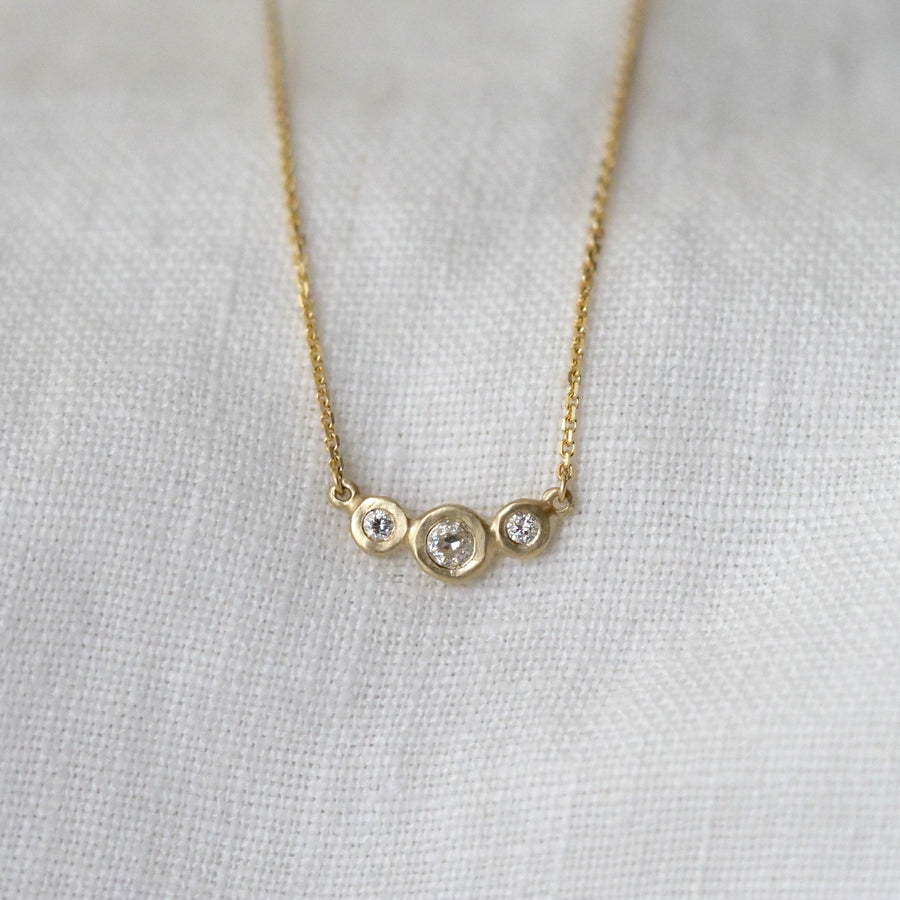 Gold necklace with three small round diamonds on a light gray background