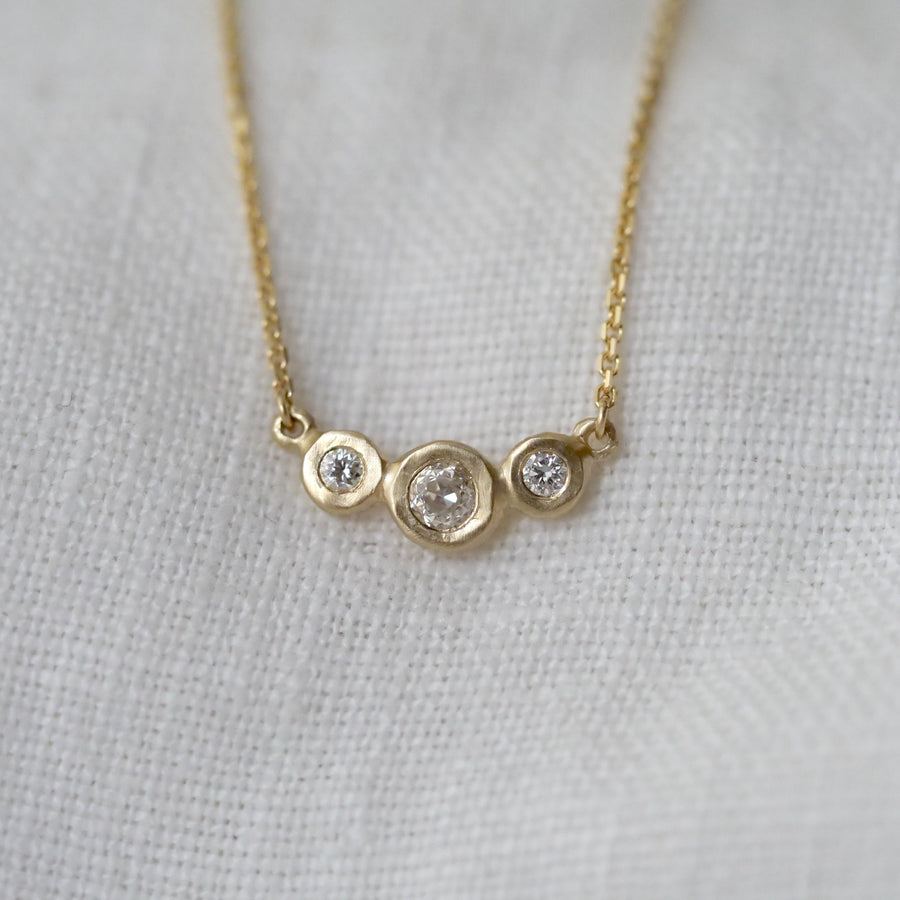 Gold necklace with three circular gemstones on a light gray background