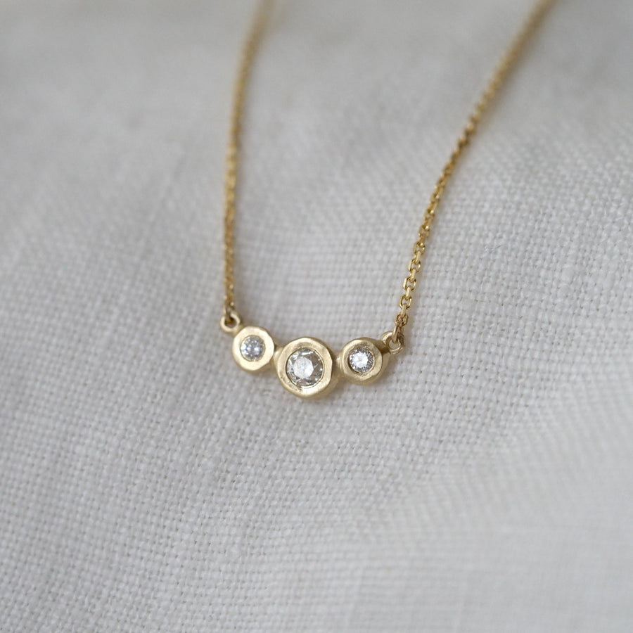 Gold necklace with three circular pendants on a light gray fabric background