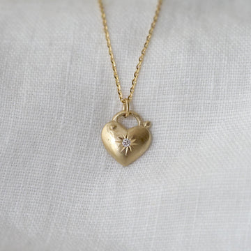 Gold heart-shaped lock necklace with a star set diamond design on a light gray background
