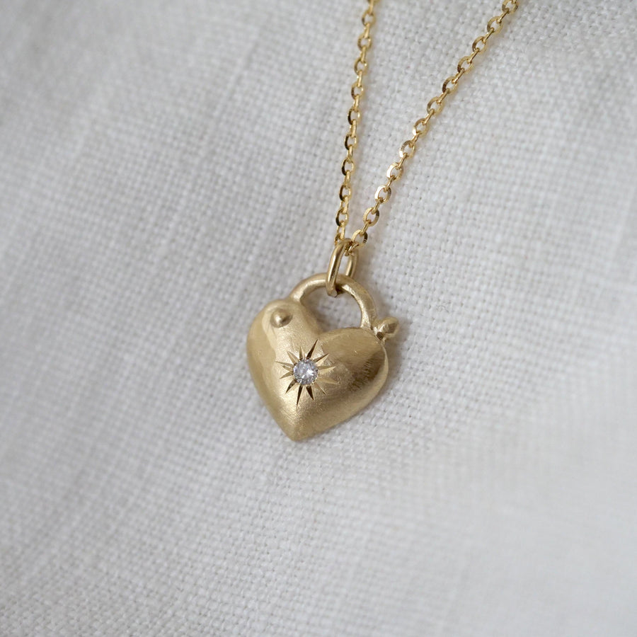 Gold heart-shaped necklace with a central gemstone on a light gray background