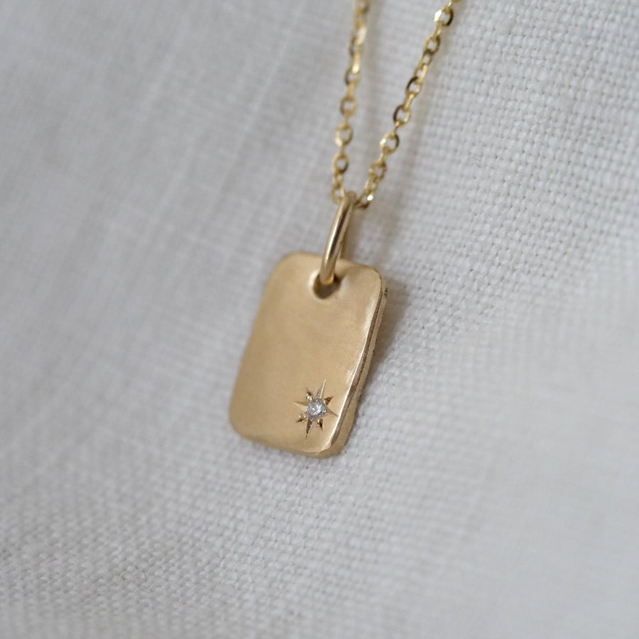 Gold necklace with a tag pendant featuring a diamond on a light gray background