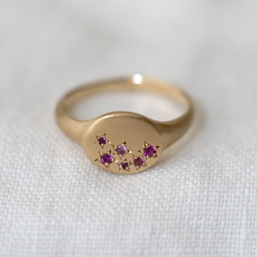 Gold ring with small pink stones on a white fabric background