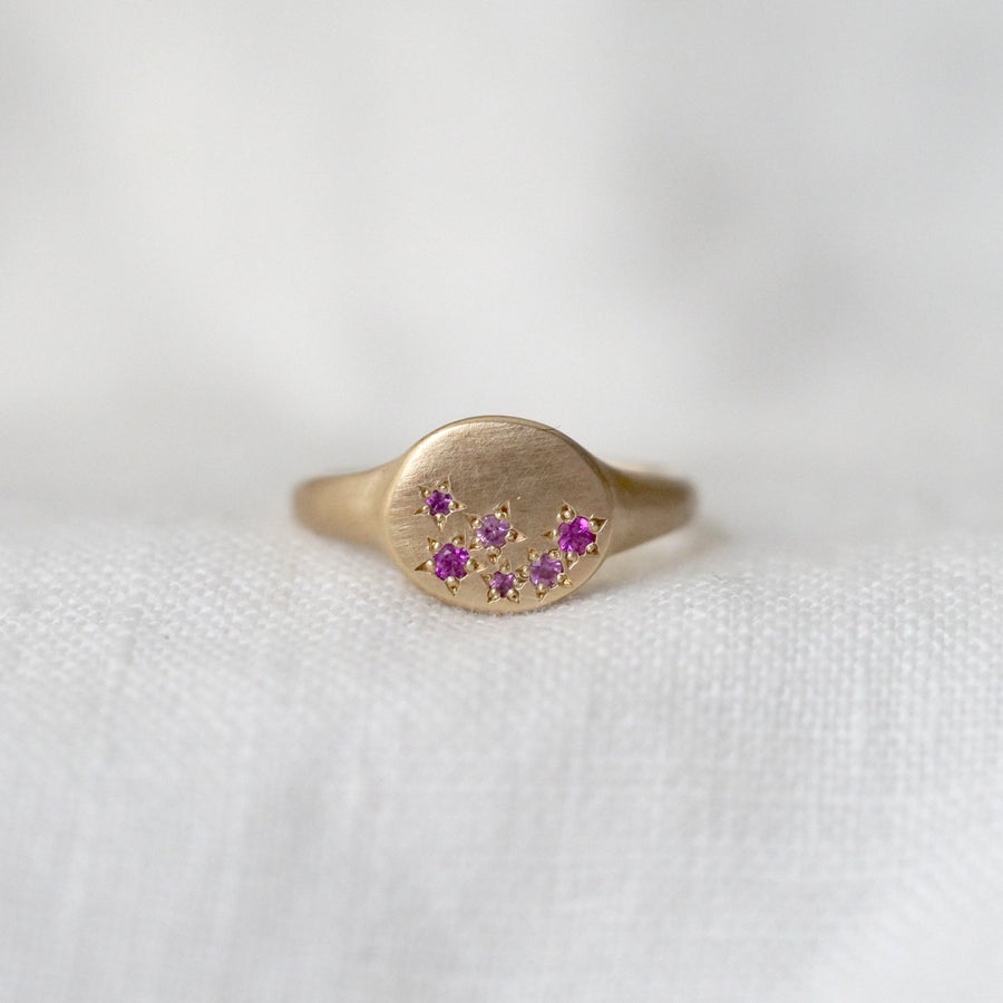 Gold signet ring with 6 star set pink sapphires on a white fabric background