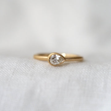 Gold ring with a pear shape diamond, bezel set east west, on a white fabric background