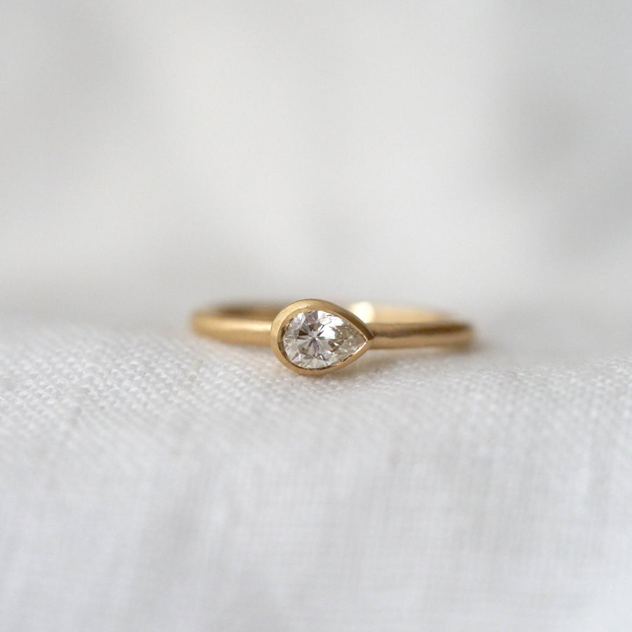 Gold ring with a pear shape diamond, bezel set east west, on a white fabric background