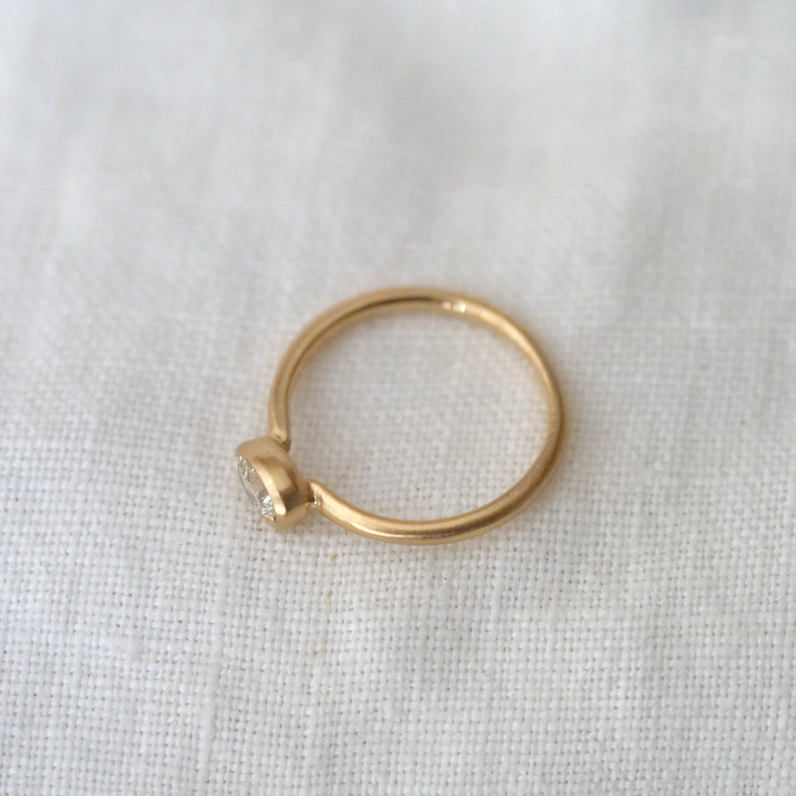 Gold ring with a small heart-shaped diamond on a white fabric background