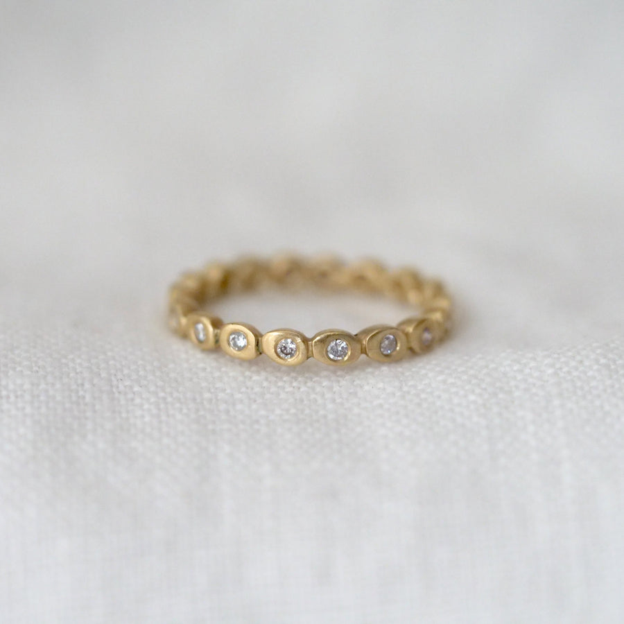 Gold ring with small diamonds bezel set all around it on a light fabric background