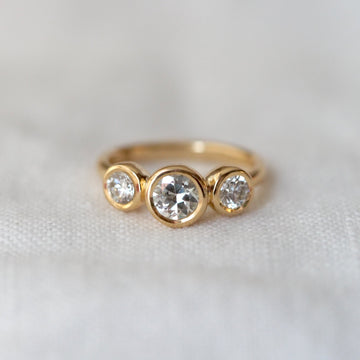 Gold ring with three round diamonds on a light fabric background
