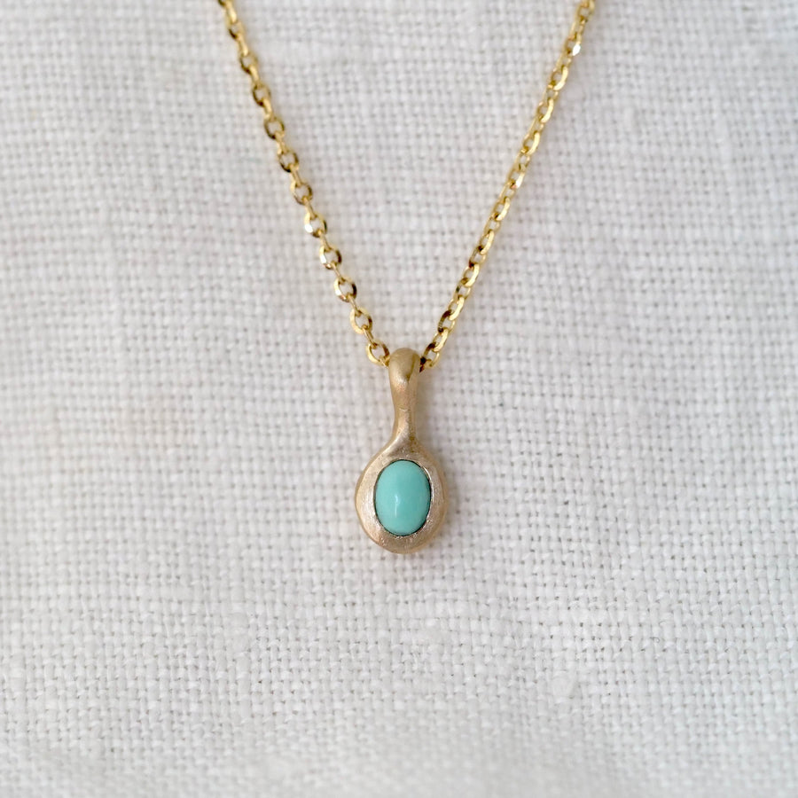 Gold necklace with a turquoise pendant on a light fabric background