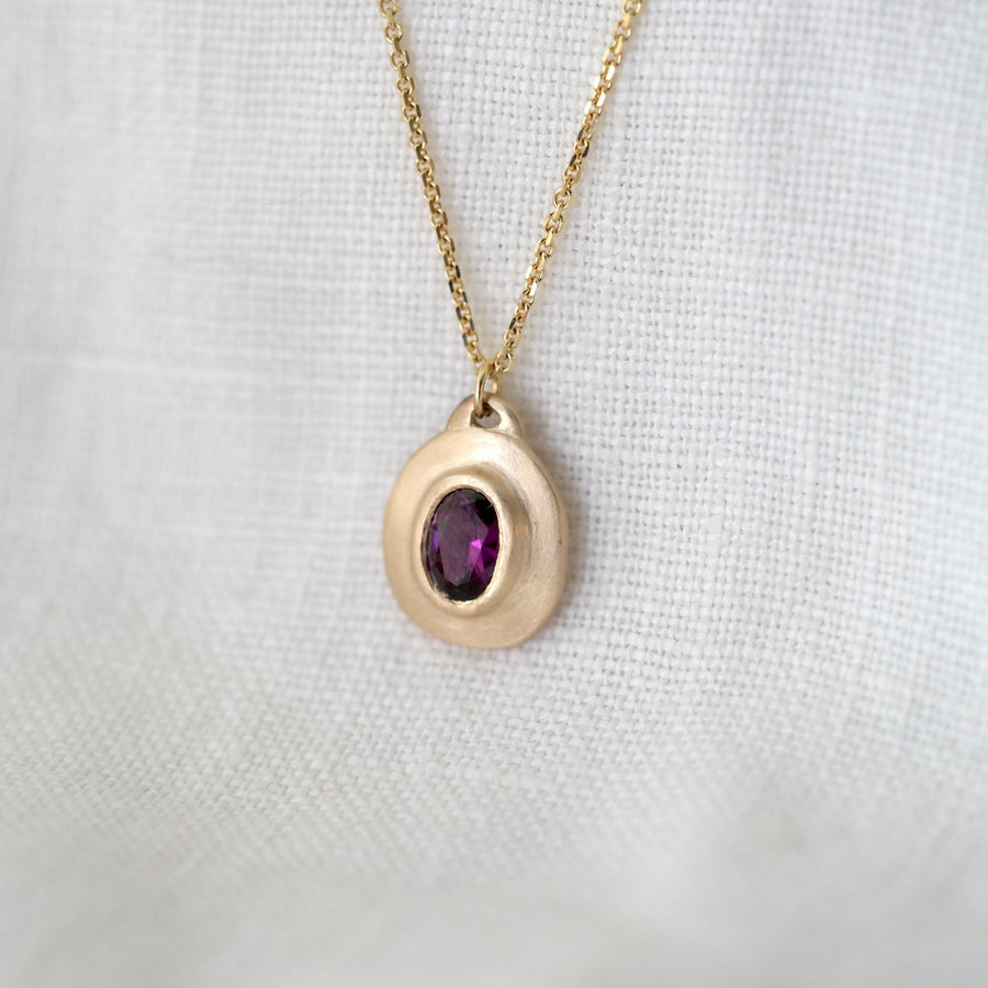 Gold necklace with a purple gemstone pendant on a white fabric background