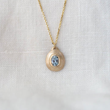 Gold necklace with a pendant featuring a blue gemstone on a white fabric background
