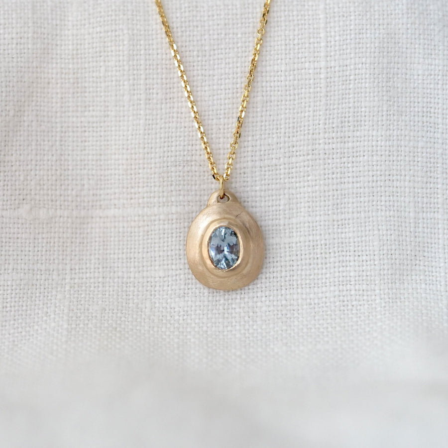 Gold necklace with a pendant featuring a blue gemstone on a white fabric background