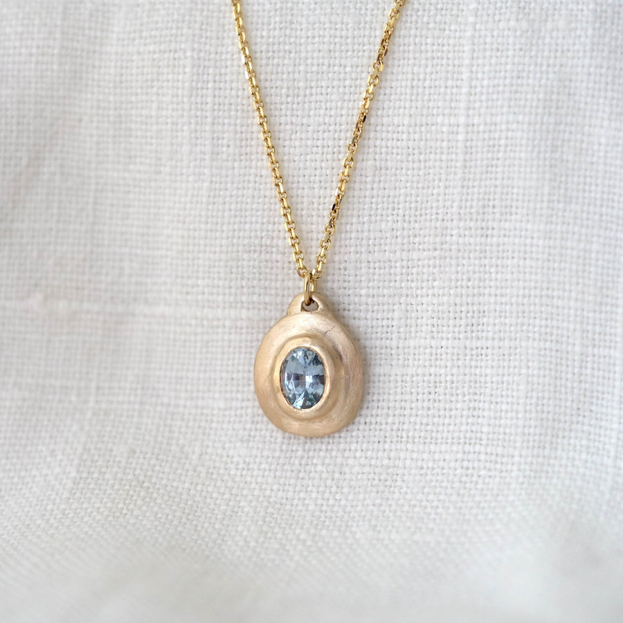 Gold necklace with a pendant featuring a blue gemstone on a white fabric background