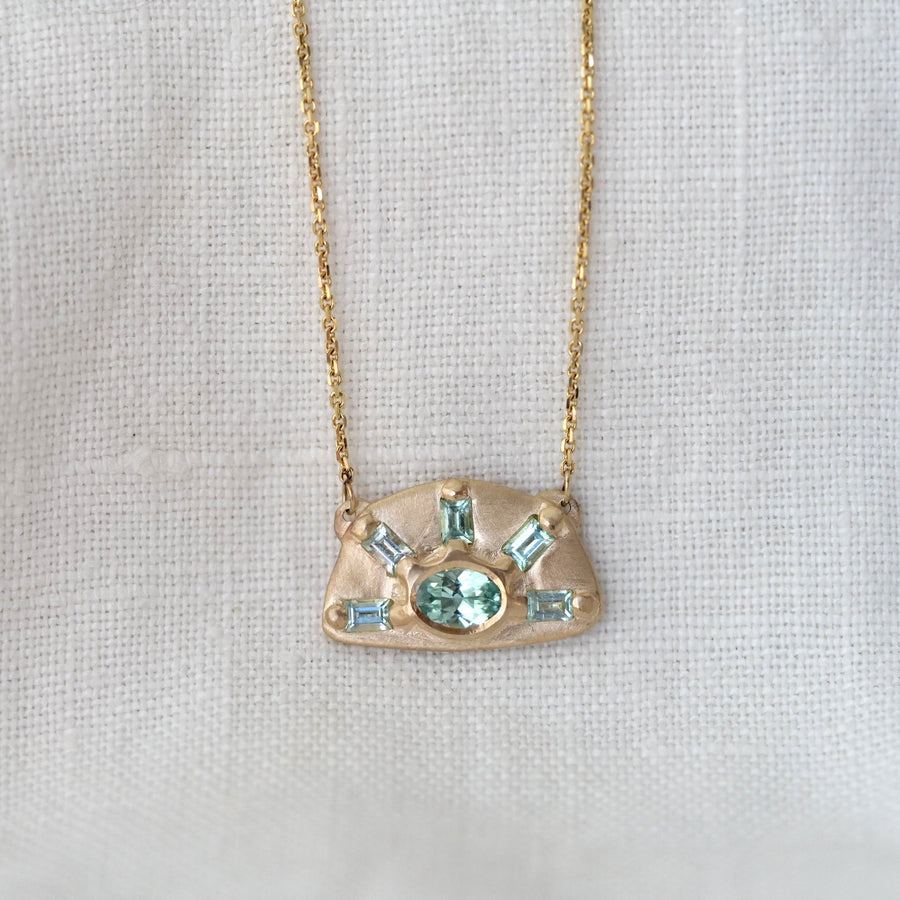 Gold necklace with a pendant featuring green gemstones on a light gray background
