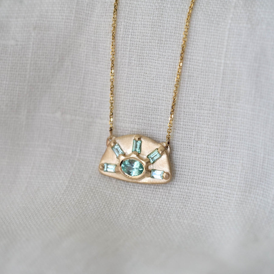 Gold necklace with a pendant featuring green gemstones on a light gray background