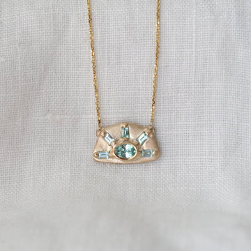 Gold necklace with a pendant featuring green gemstones on a light gray background