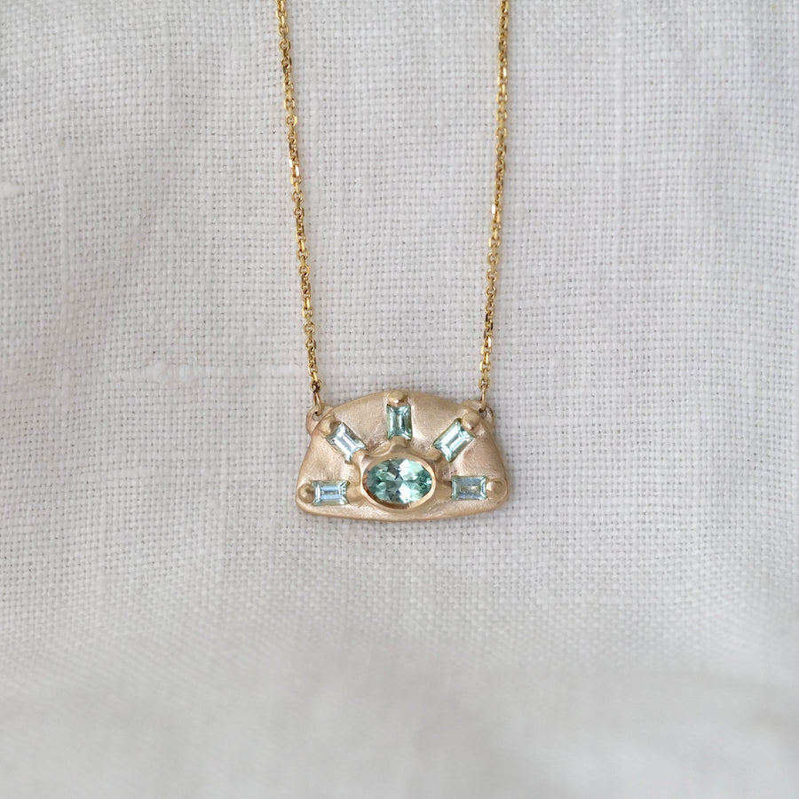 Gold necklace with a pendant featuring green gemstones on a light gray background