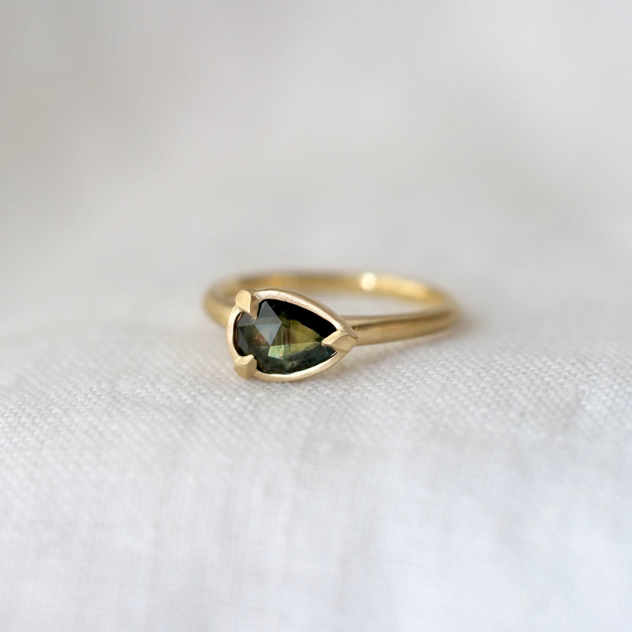 Gold ring with a green gemstone on a white fabric background