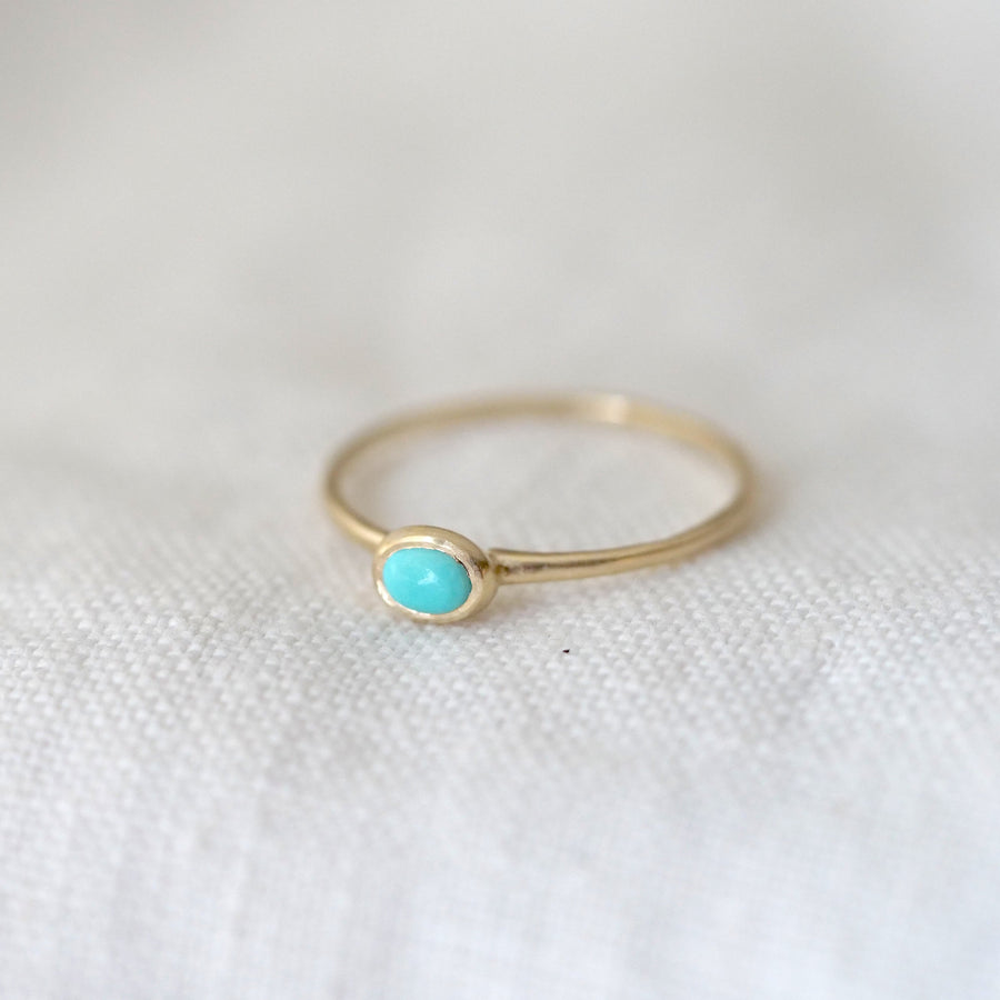 Gold ring with a turquoise stone on a white fabric background
