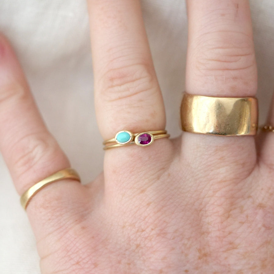 Hand wearing gold rings with gemstones on a neutral background
