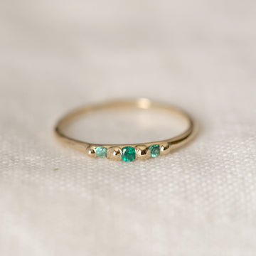 Gold ring with emerald stones on a light background