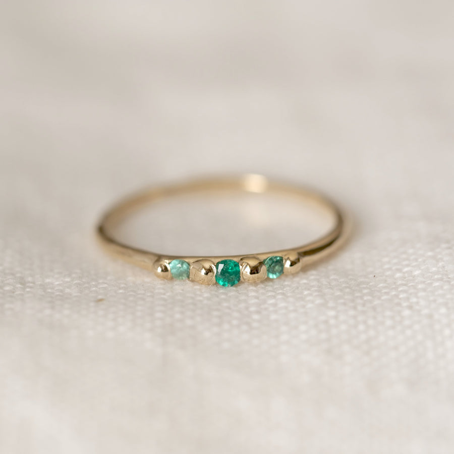 Gold ring with emerald stones on a light background