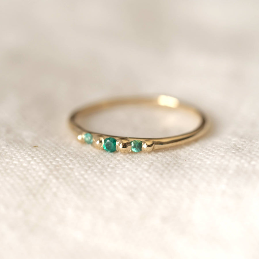 Gold ring with emerald stones on a textured white surface