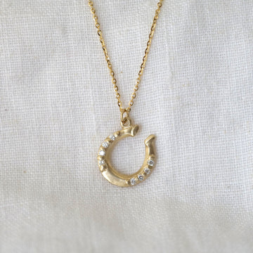 Gold horseshoe necklace with white diamonds on a white fabric background