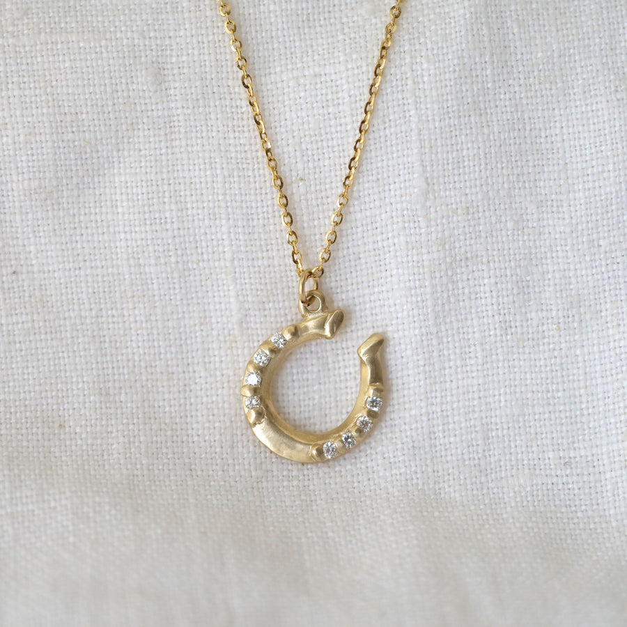 Gold horseshoe necklace with white diamonds on a white fabric background