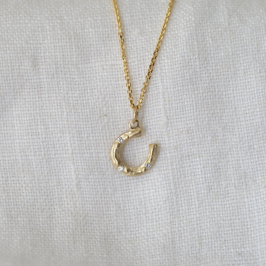 Little Gold horseshoe necklace with three diamonds on a light gray fabric background