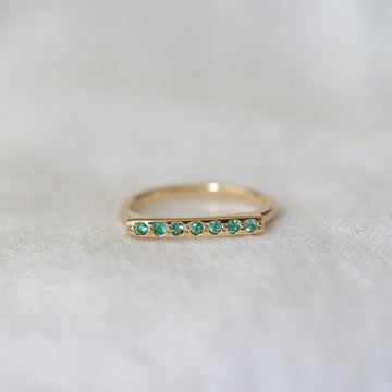 Gold ring with emerald stones on a light gray background