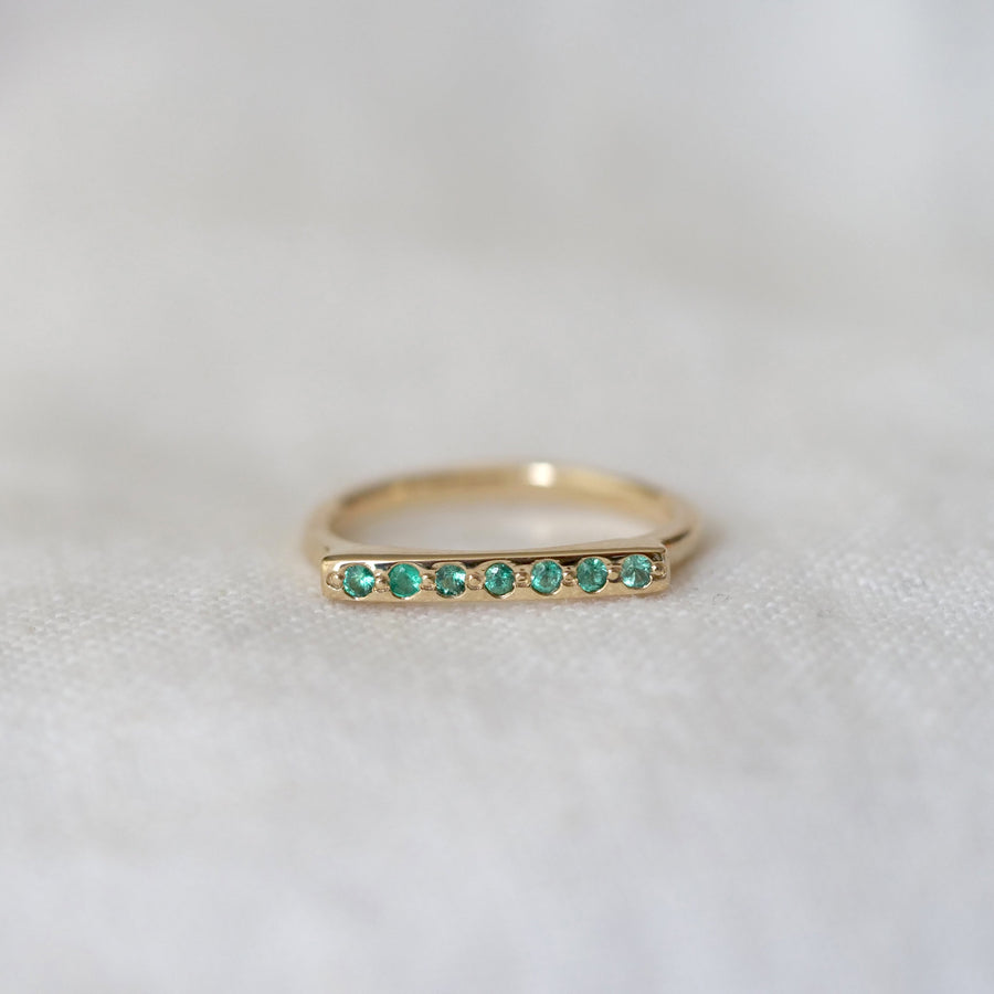 Gold ring with emerald stones on a light gray background