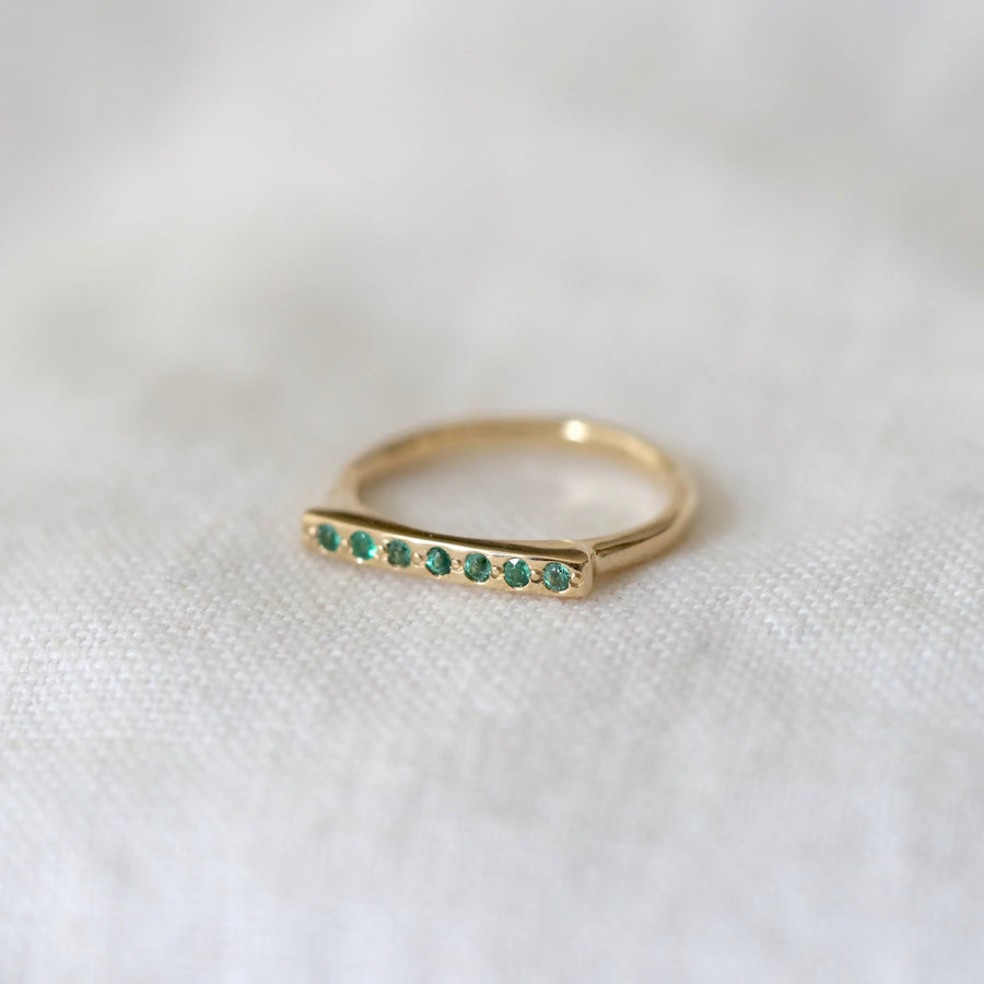 Gold ring with green gemstones on a white fabric background