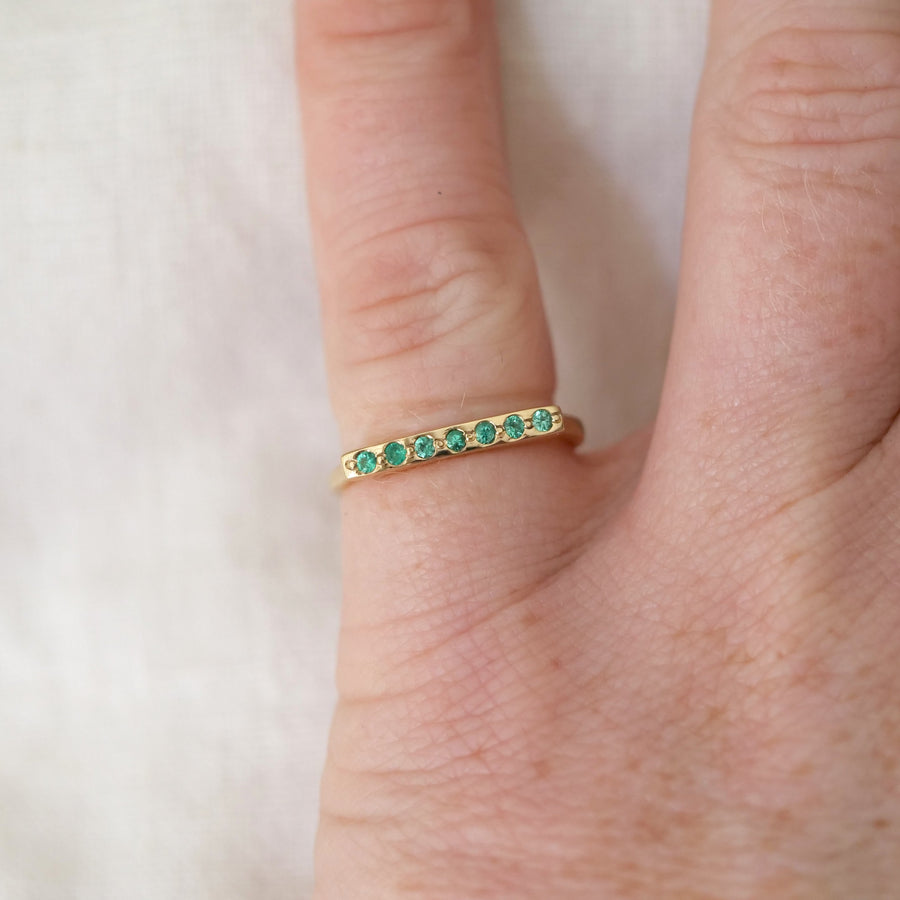 Gold ring with green gemstones on a finger against a white background