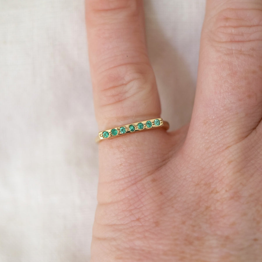 Gold ring with green gemstones on a finger against a light background