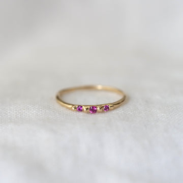 Gold ring with three pink gemstones on a white background