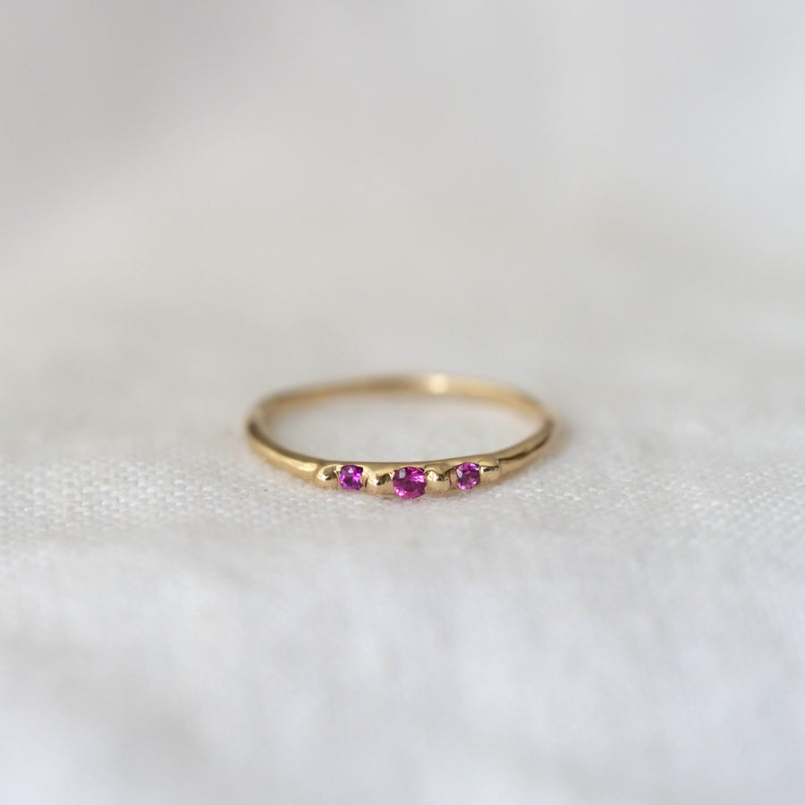 Gold ring with three pink gemstones on a white background