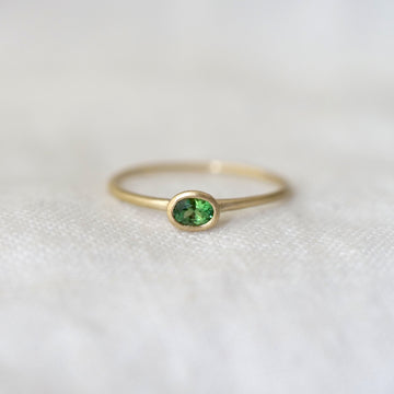Gold ring with an oval green gemstone on a white background