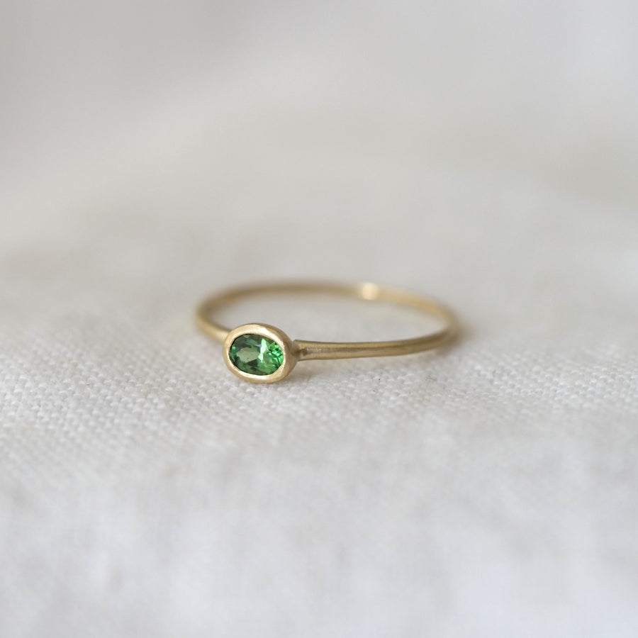 Gold ring with a green gemstone on a white fabric background