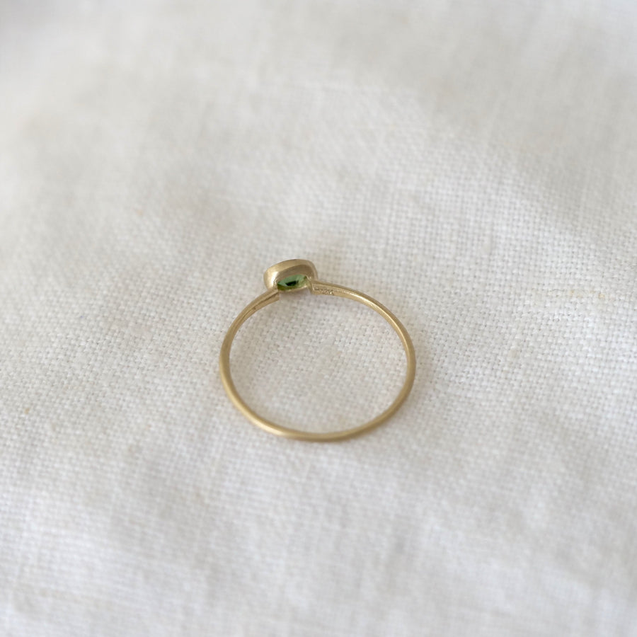 Gold ring with a green gemstone on a white fabric background