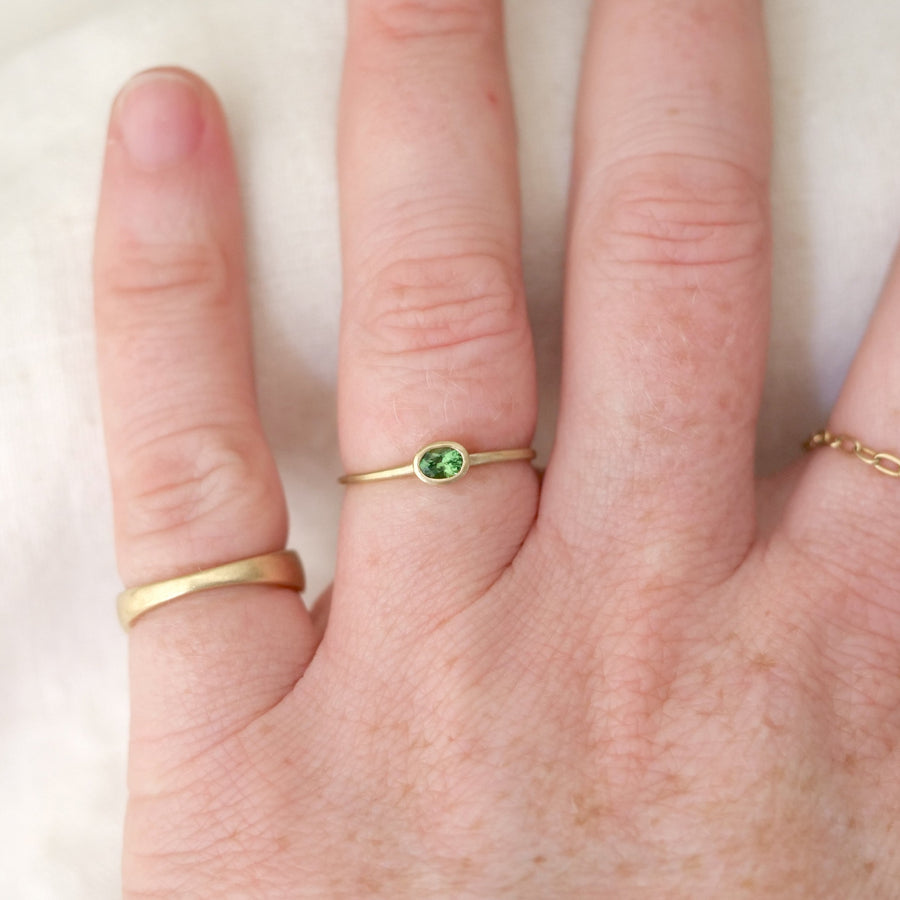 Gold ring with a green gemstone on a finger against a white background