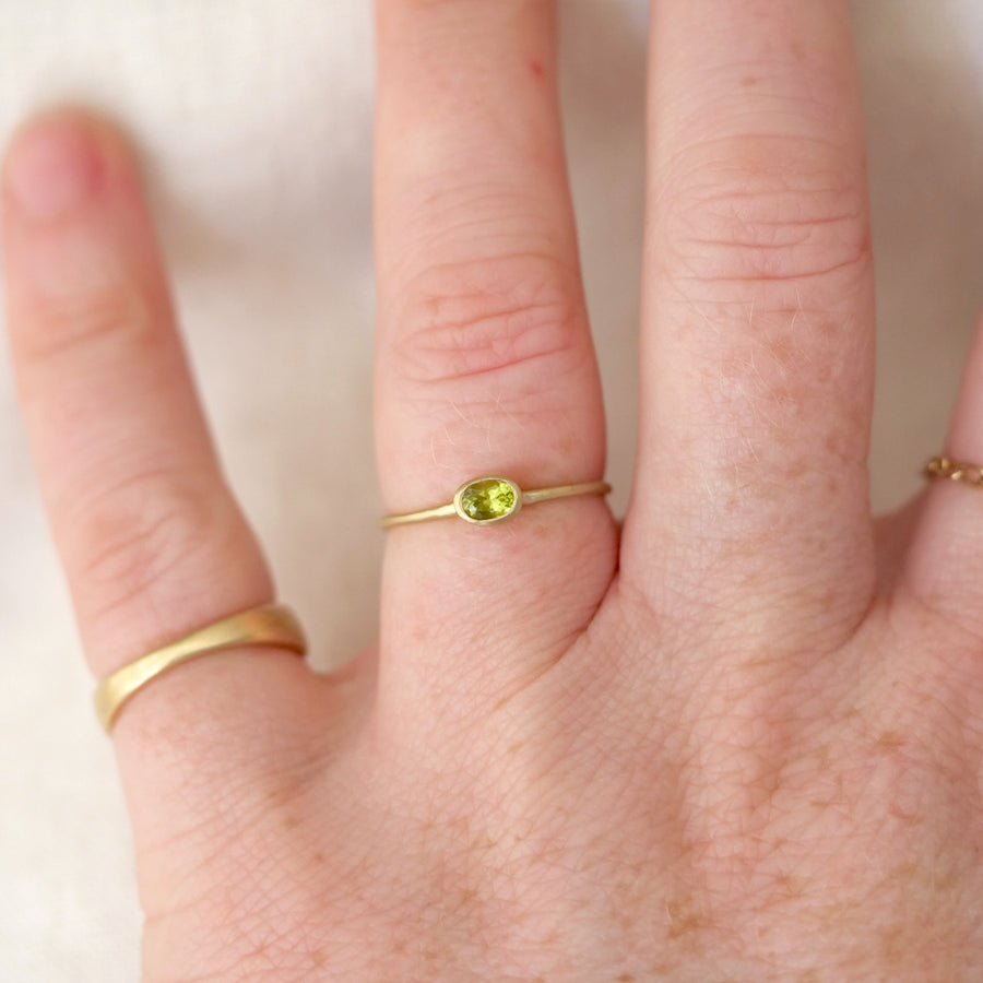 Hand wearing a gold ring with a green gemstone on a neutral background
