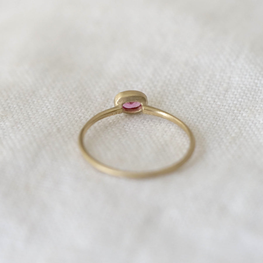 Gold ring with a pink gemstone on a white textured fabric background