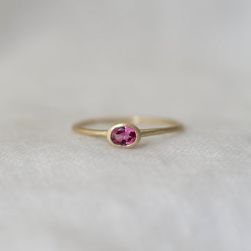 Gold ring with a pink gemstone on a light gray background