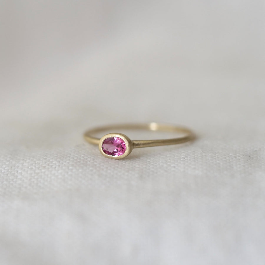 Gold ring with a pink gemstone on a light gray background
