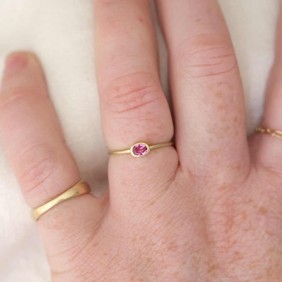 Gold ring with a pink gemstone on a person's finger against a white background