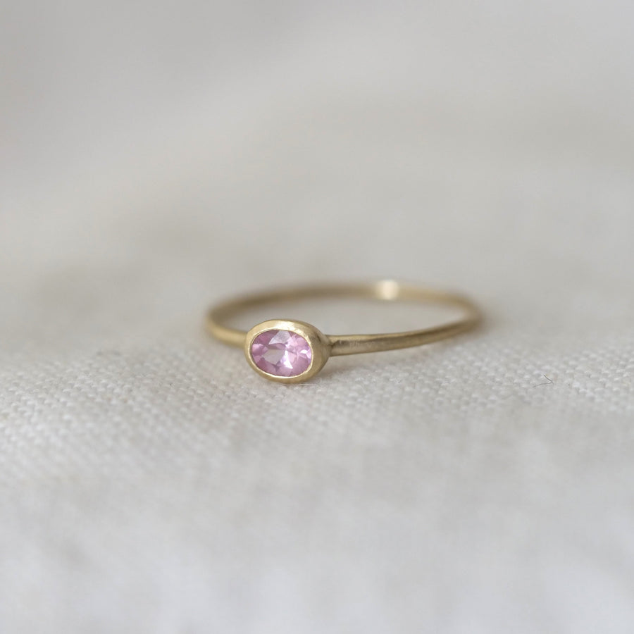Gold ring with a pink gemstone on a light fabric background