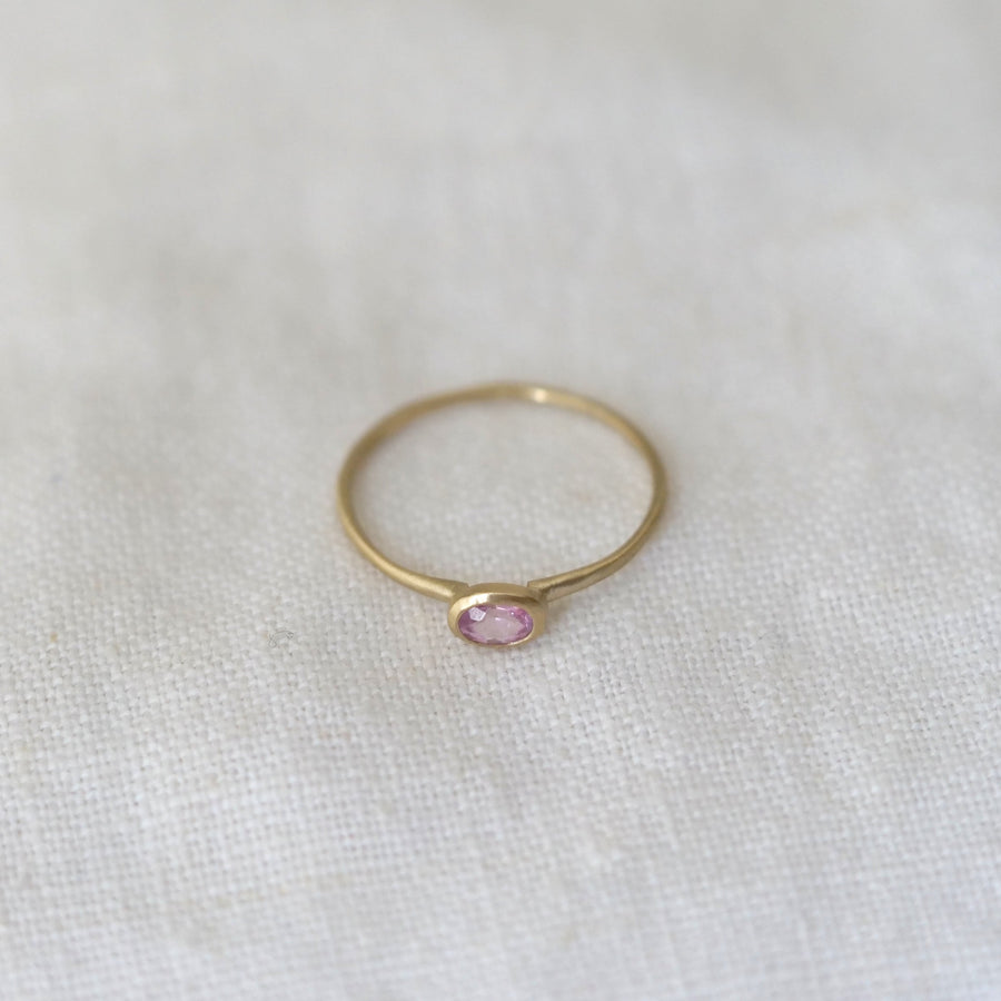 Gold ring with a light pink gemstone on a white fabric background