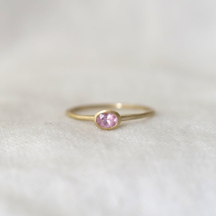 Gold ring with a pink gemstone on a light gray background